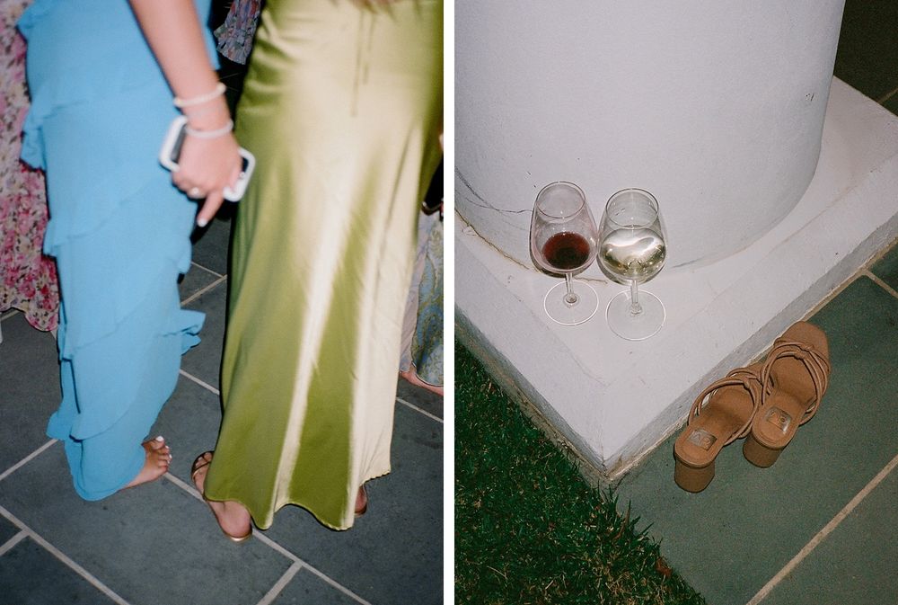 Two party guests in elegant gowns stand next to abandoned wine glasses and sandals on a patio.