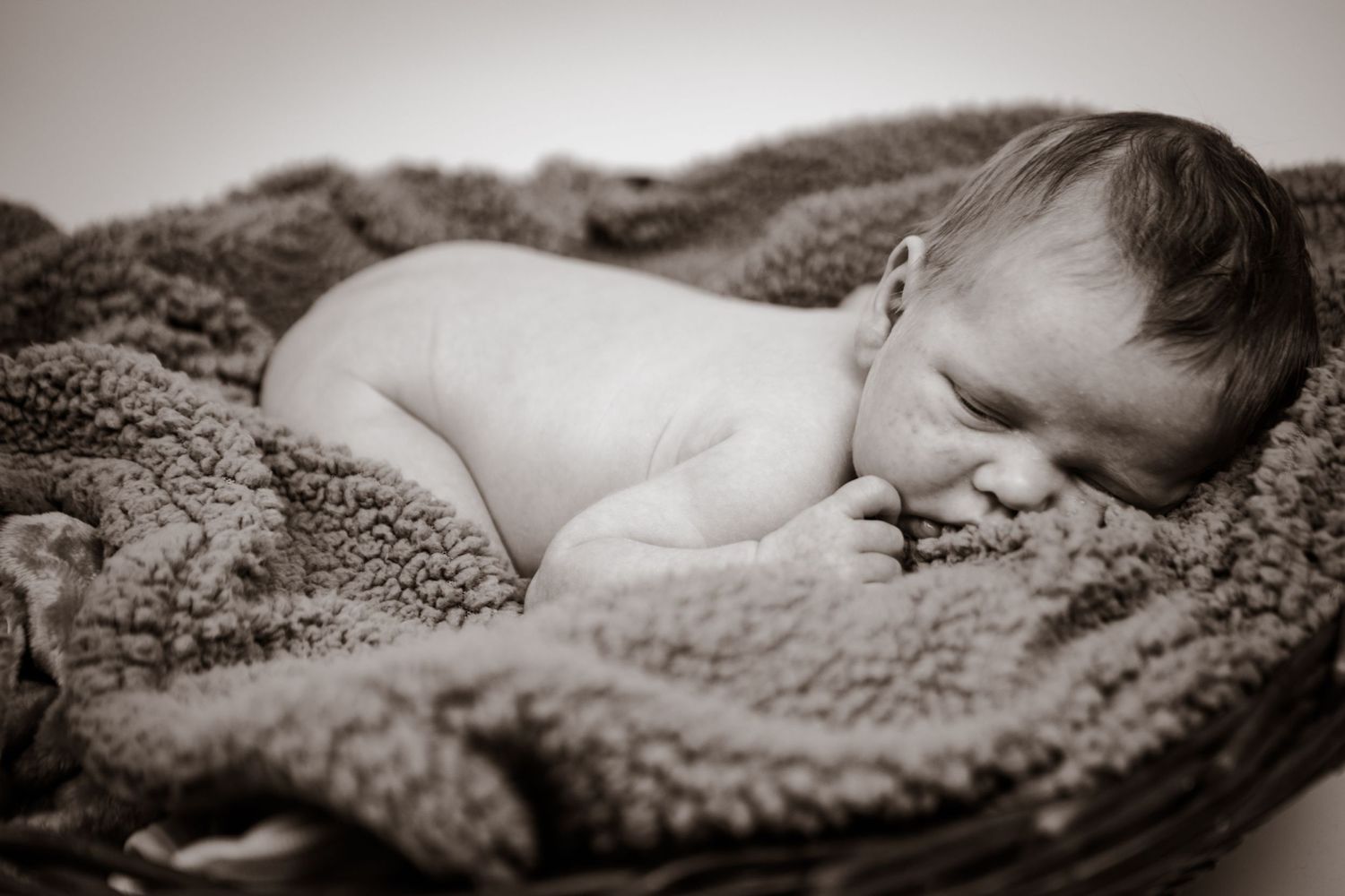 Black and white portrait of a sleeping baby nestled peacefully in soft textured blankets.