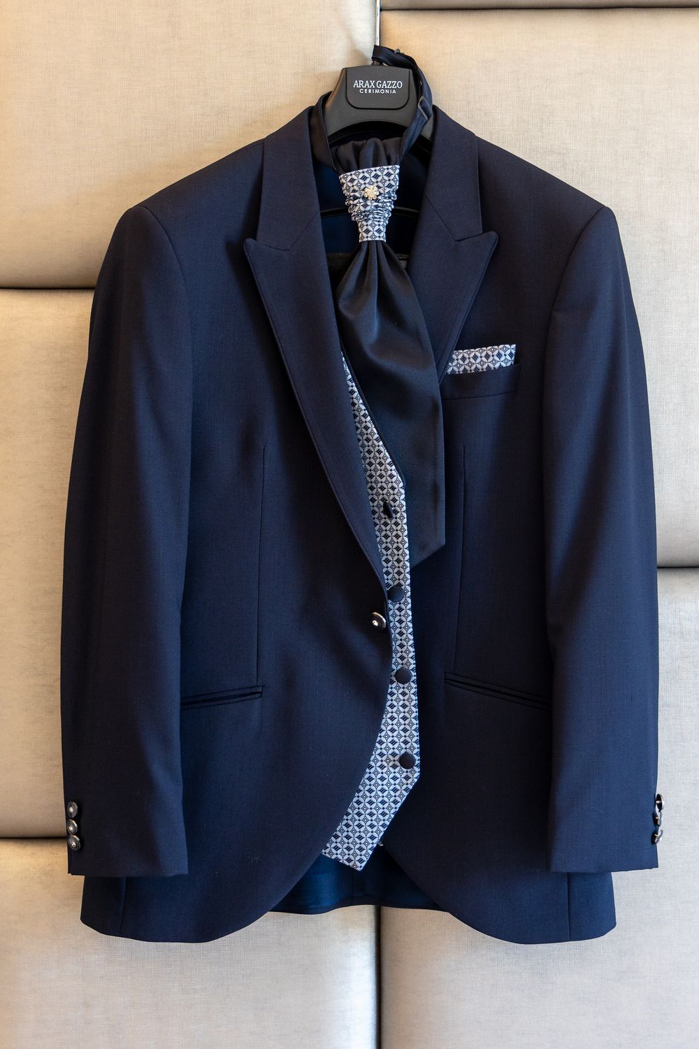 Navy blue suit jacket and patterned tie hanging on display against light colored background.