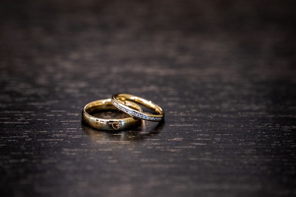 Close-up of two gold wedding rings with diamonds on dark wooden surface.