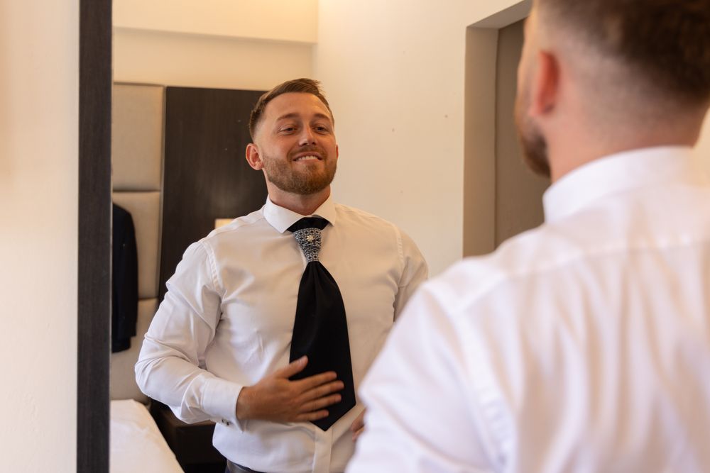 Person in white dress shirt and tie looking in mirror while getting ready.