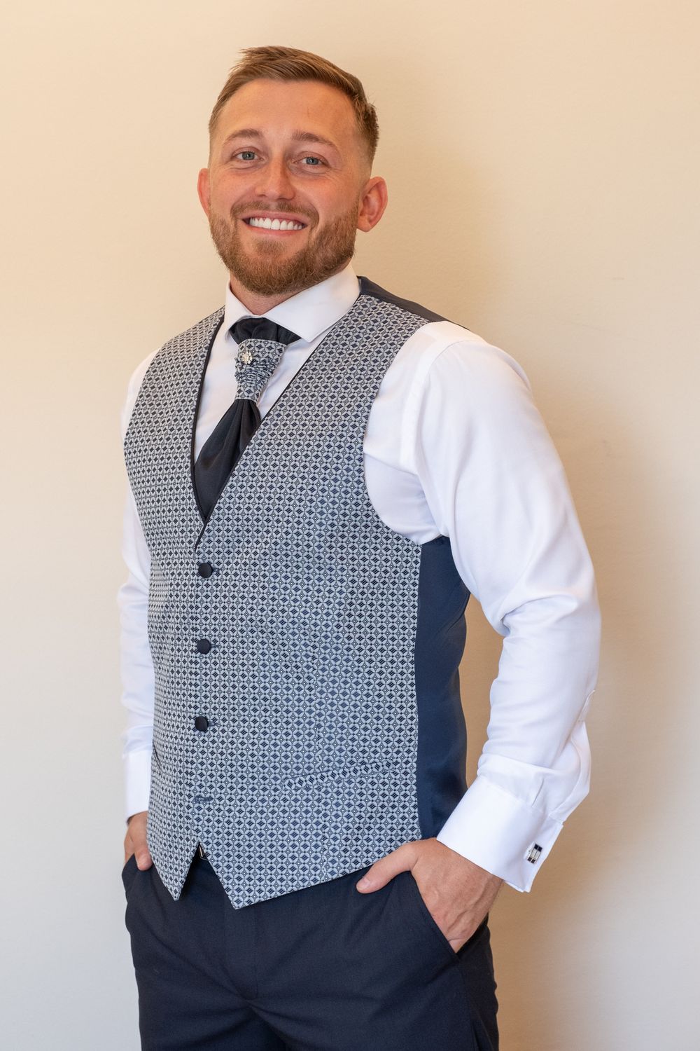 Formal three piece suit ensemble with patterned grey vest and navy trousers.