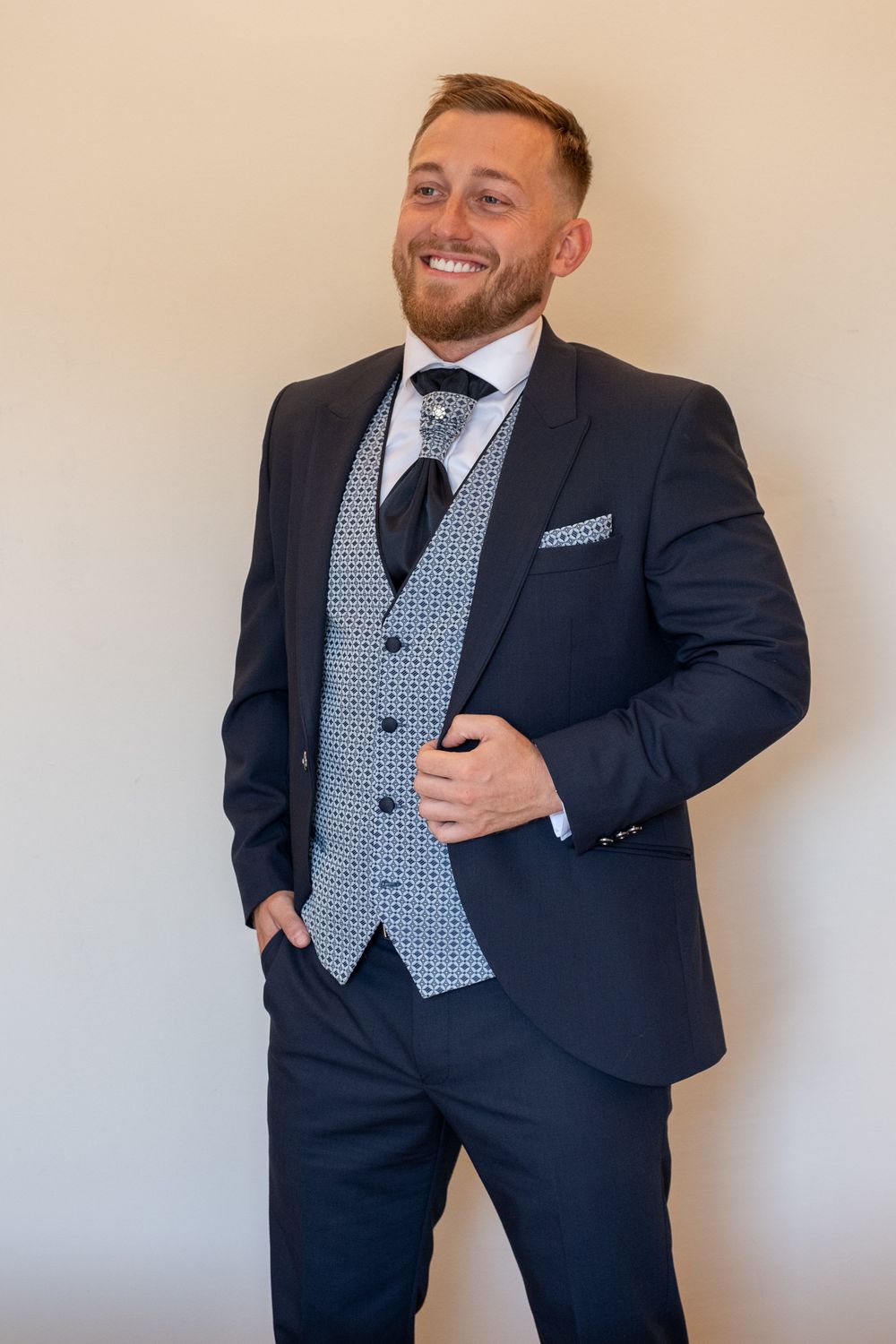 Groom poses in stylish navy three-piece suit with patterned grey waistcoat and pocket square.