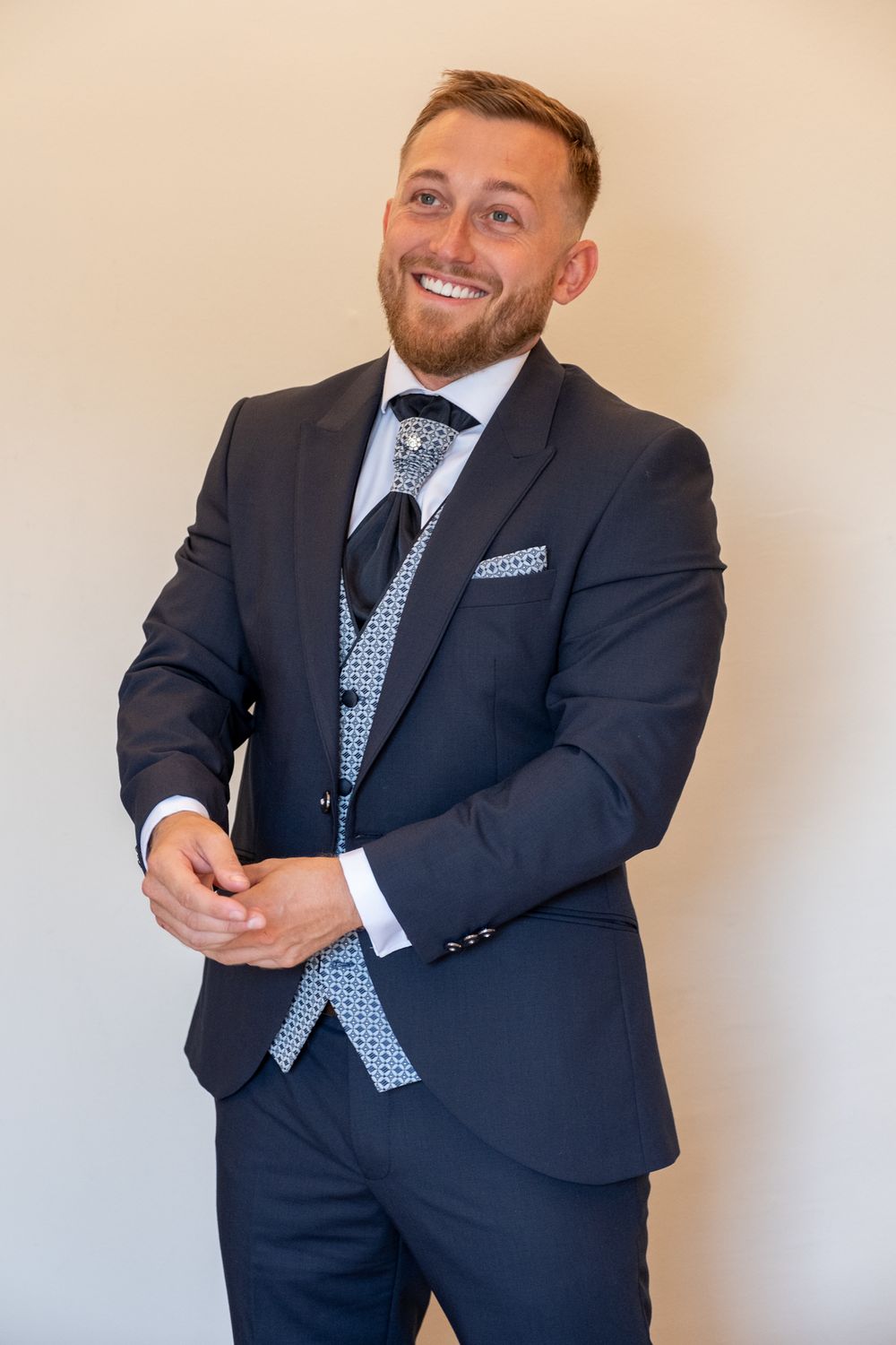 Elegant formal attire featuring navy suit jacket and light patterned waistcoat against neutral background.