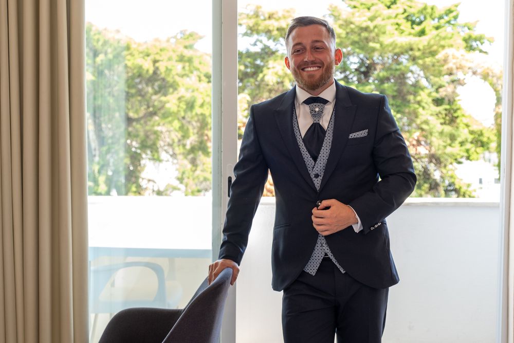 Formal suited figure stands confidently by bright window in modern interior setting.