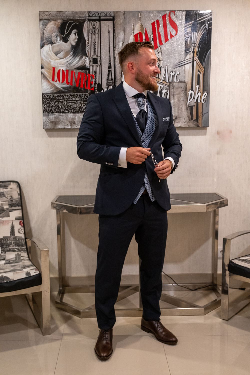 Well-dressed figure poses in navy suit against artistic wall decor in modern space.