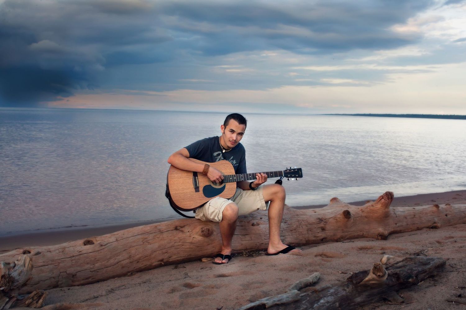 A silhouette plays an acoustic guitar at sunset by the ocean, creating a peaceful beach atmosphere.
