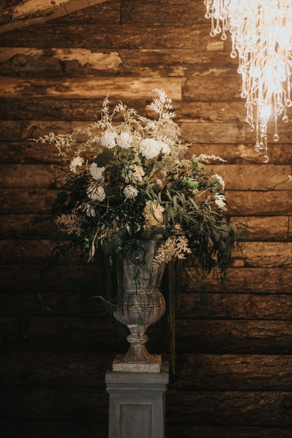 Elegant white floral arrangement in stone urn against rustic wooden wall background at Grand Lodge Oaklands - taken by Grimsby photographer.