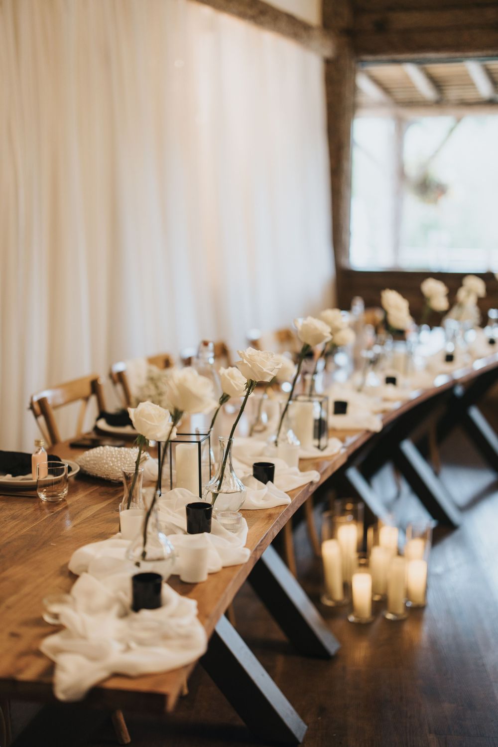 Elegant wedding reception table decorated with white roses in vases and glowing candles at Grand Lodge Oaklands.