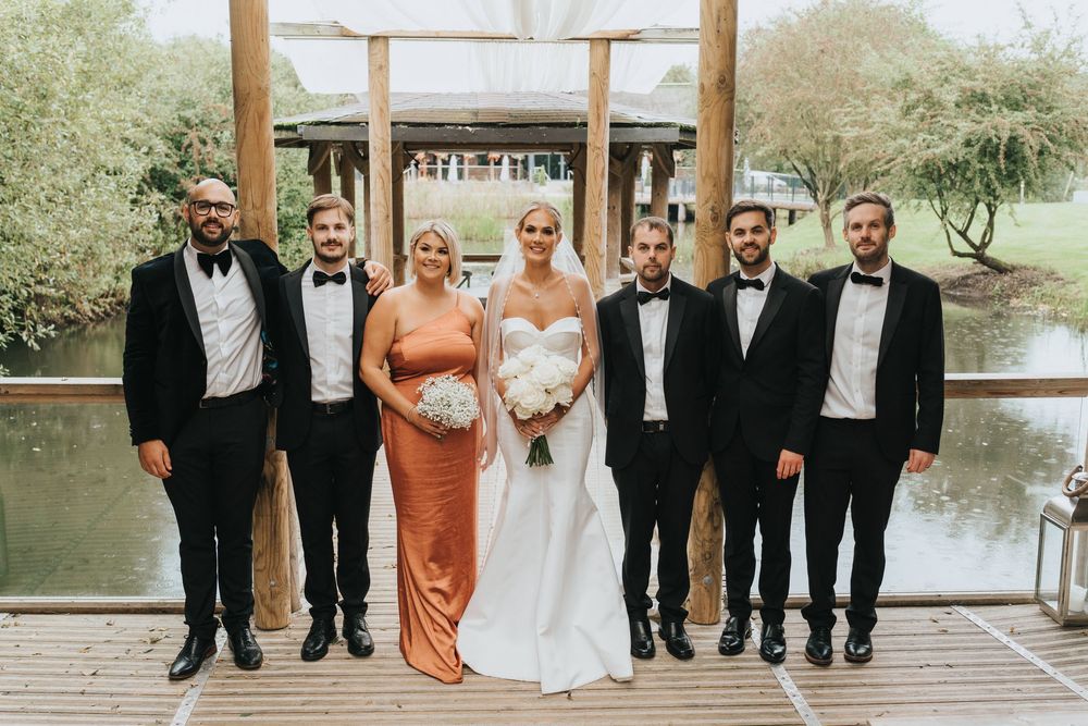 Wedding party members stand together in formal attire for photos near a scenic pond at Grand Lodge Oaklands - taken by Grimsby photographer.