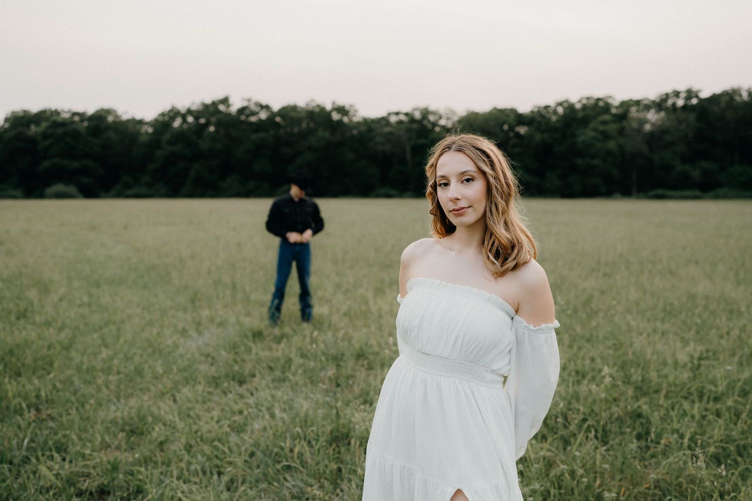 A romantic photoshoot in a serene meadow with trees in the background during golden hour.