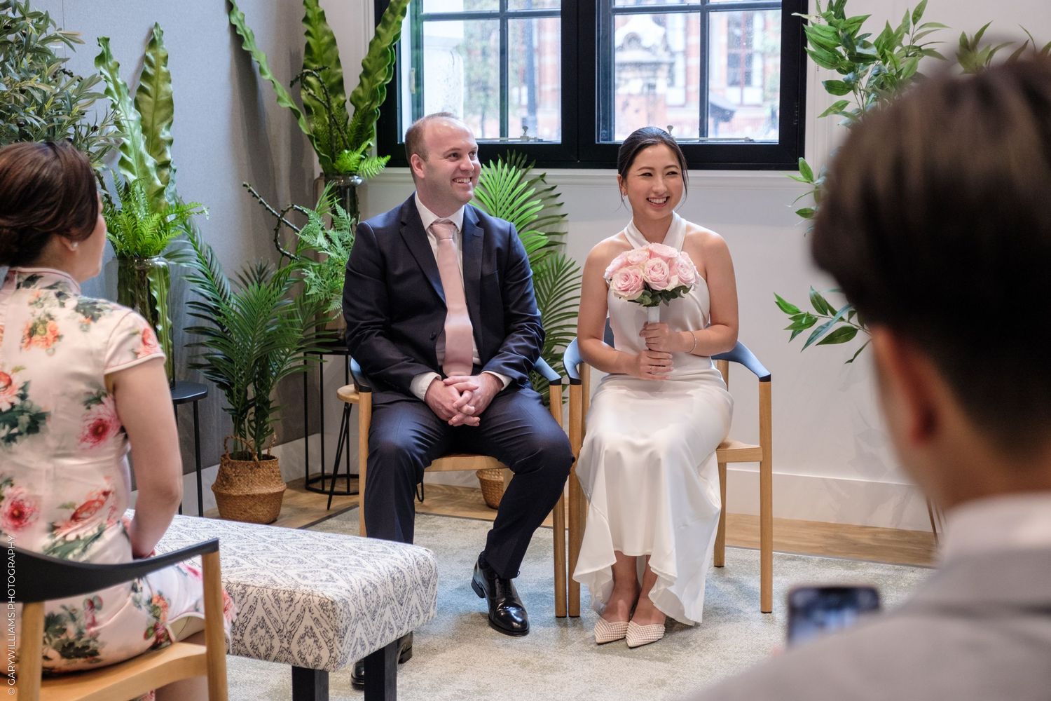 A couple sits together for an indoor Q&A session with guests surrounded by green plants and natural lighting.