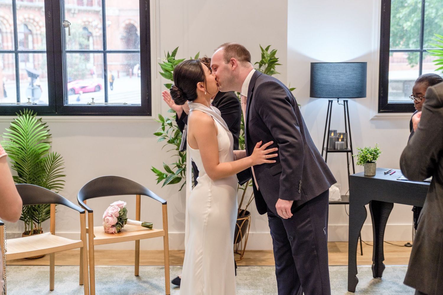 Two people share an intimate moment during a first look wedding photo session in a modern bright space with plants.
