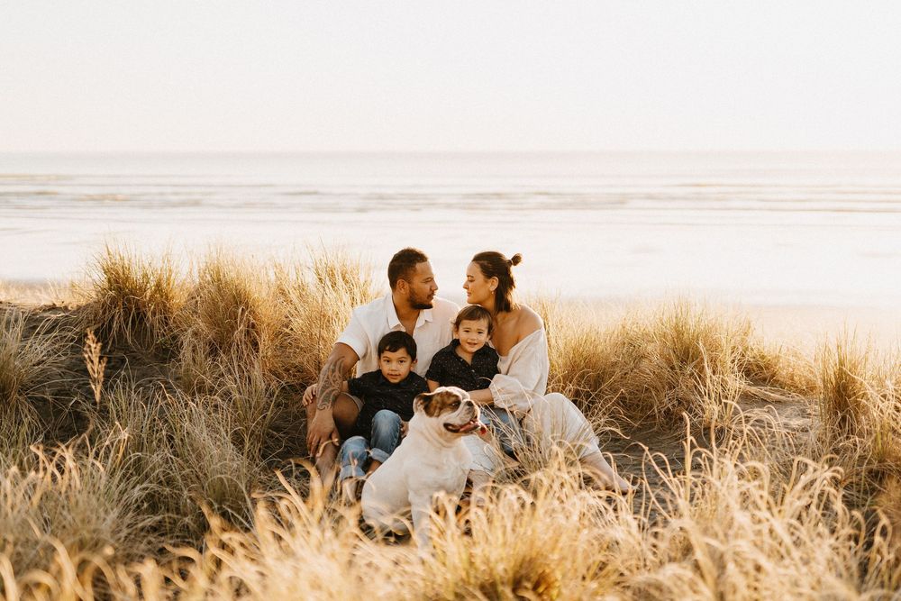 Family sits together among golden grass during sunset at a coastal viewpoint.