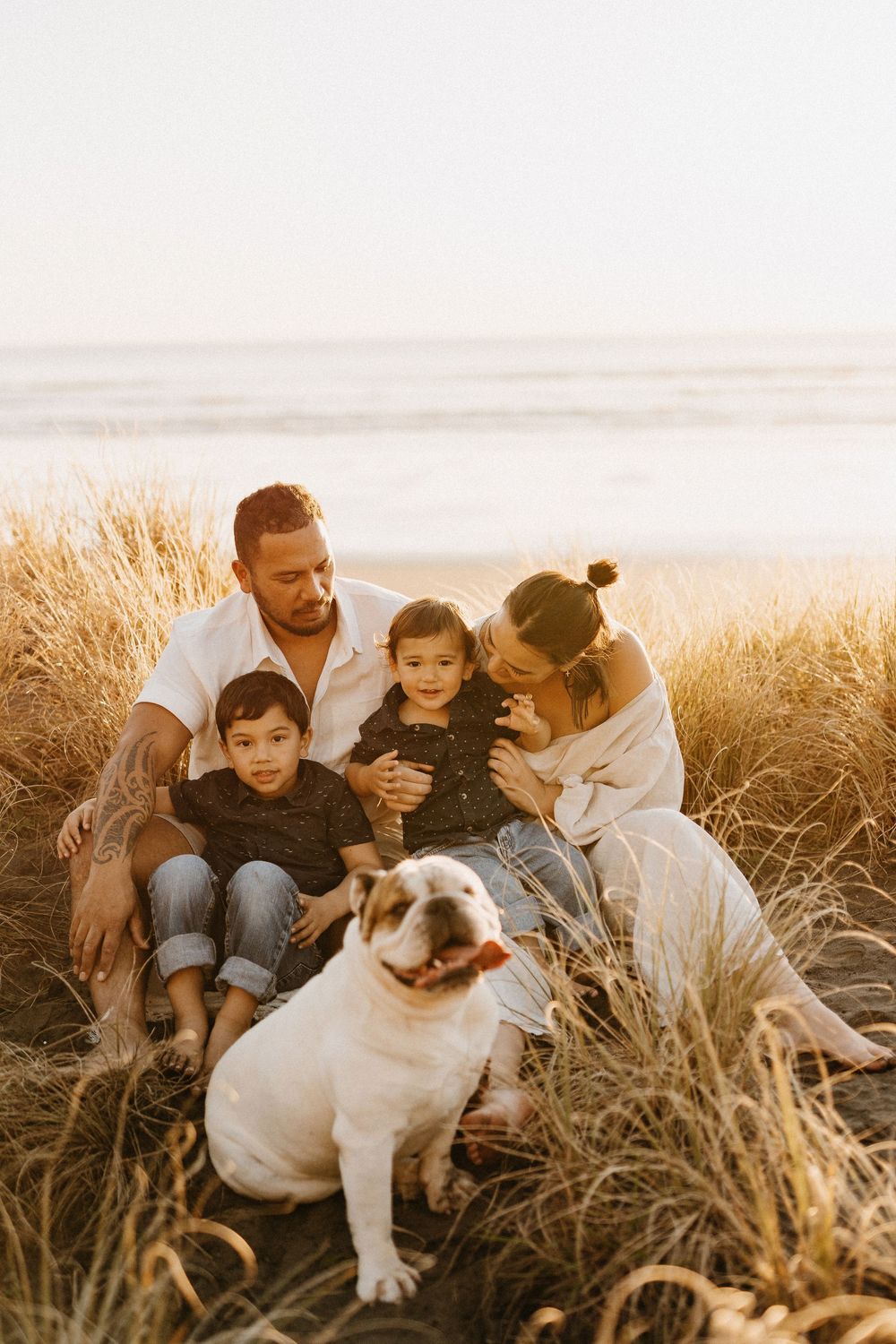 A group petting a white and brown dog while sitting in tall grass during golden hour.