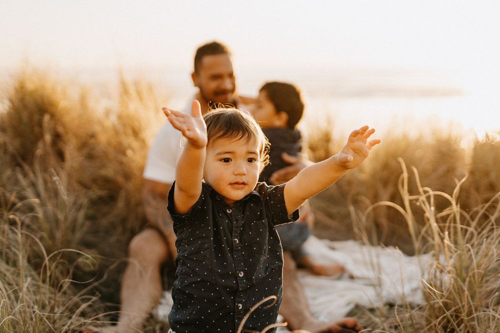 Young child plays in tall grass at sunset during golden hour creating joyful silhouette against warm sky.