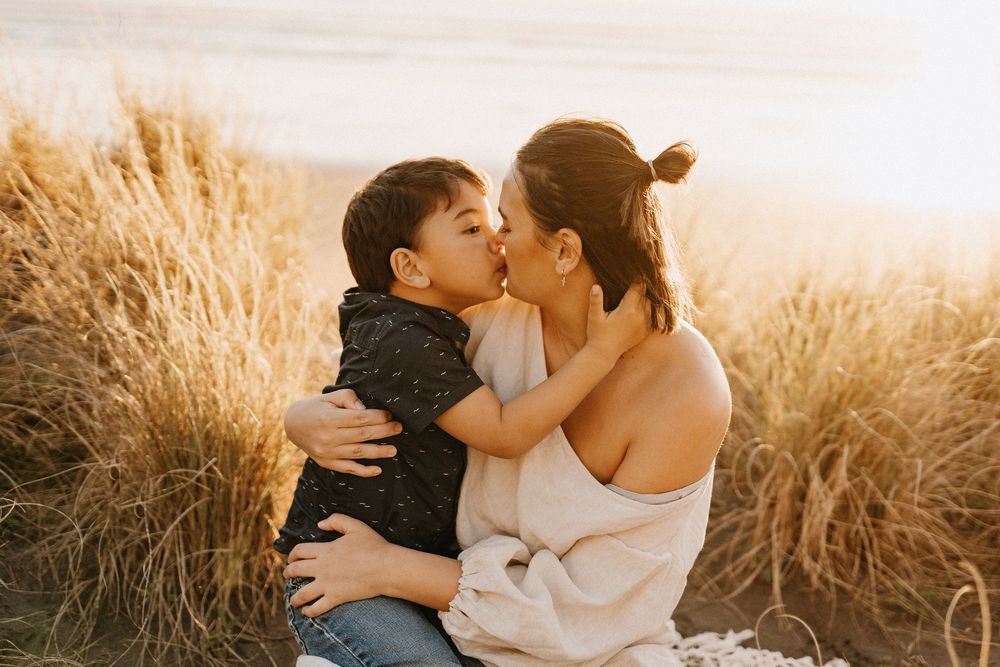 A parent and child share an affectionate moment in a sun-lit field of golden wheat during sunset.
