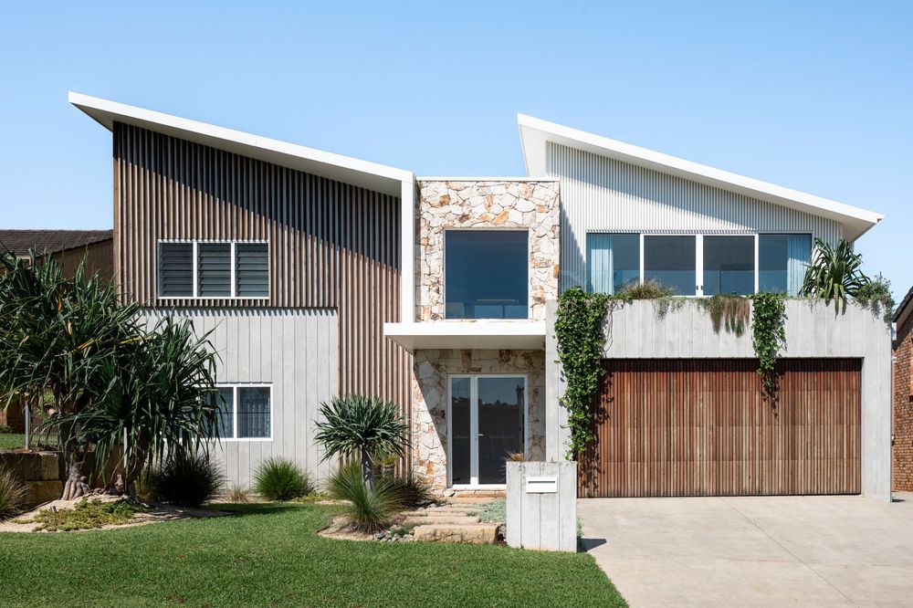 Modern two-story home with angular roofline features wood and stone facade accents, palm trees, and attached garage.