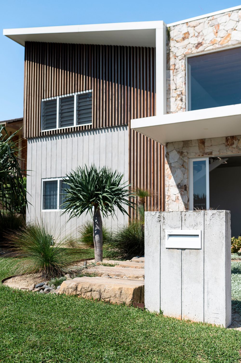 A modern white apartment building with vertical wood slats and palm trees on a grassy hillside.
