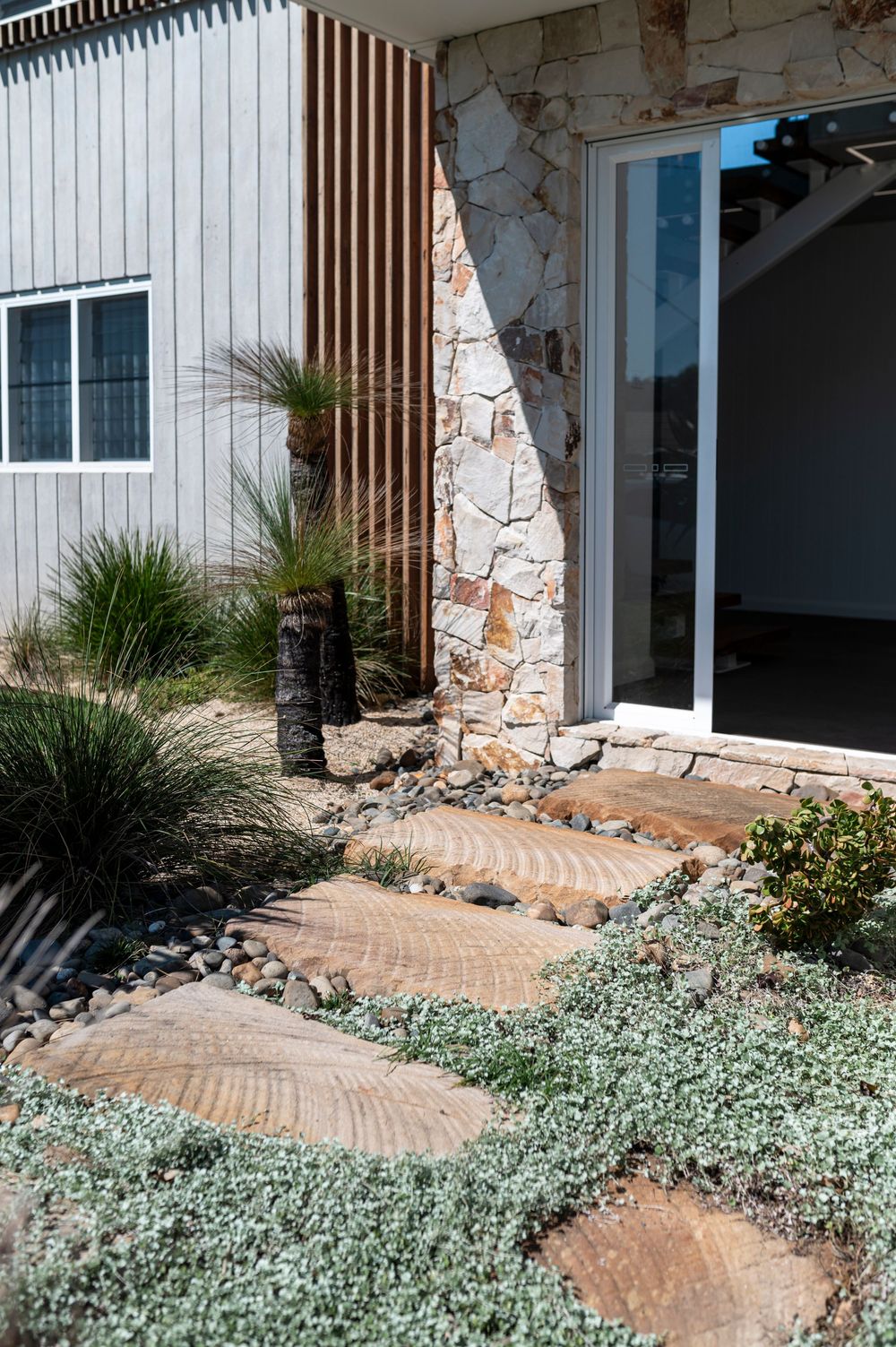 A curved brick pathway leads to an entrance, bordered by silvery ground cover plants and lush landscaping.