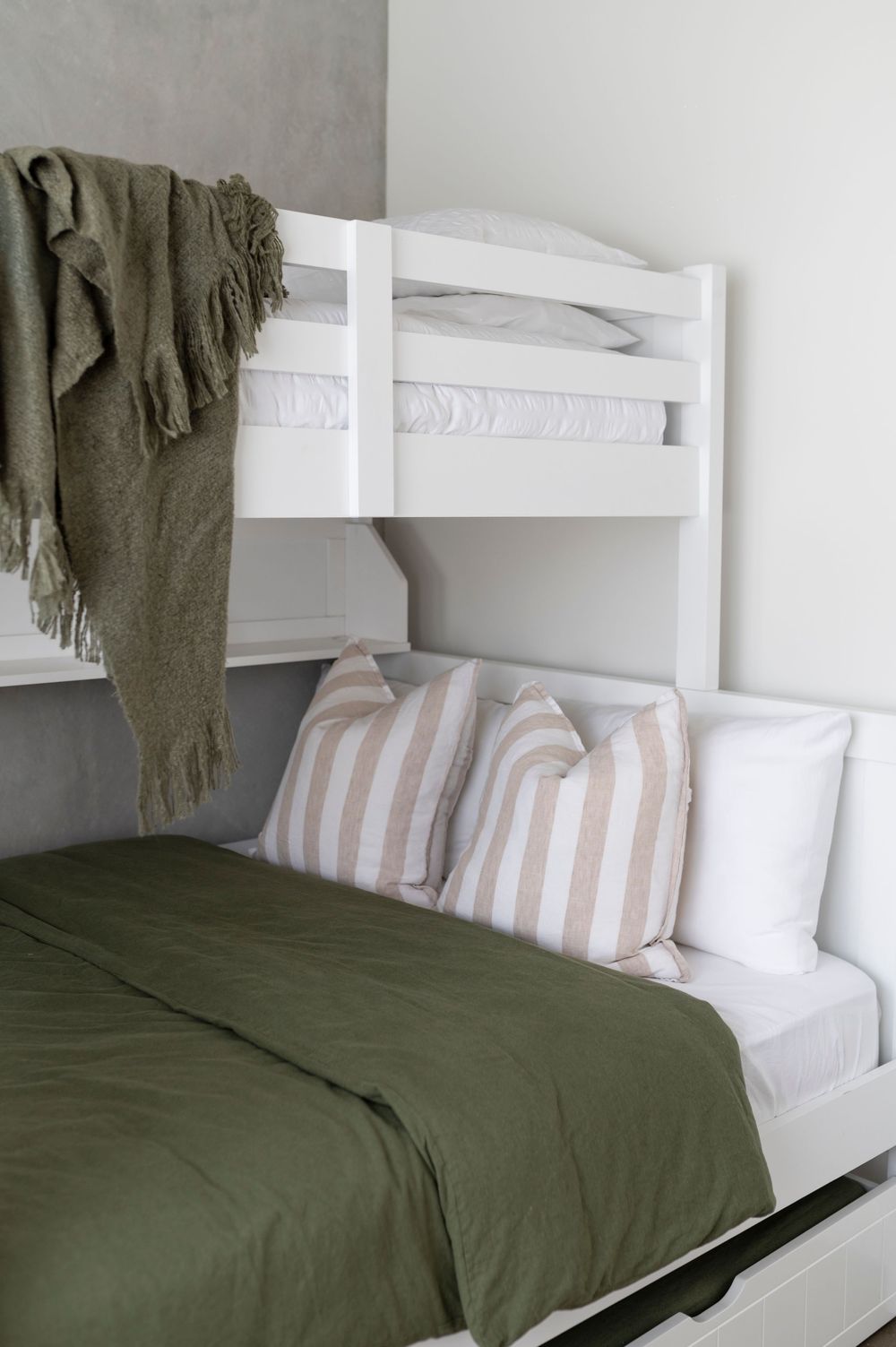 Modern bunk bed with olive green bedding, striped pillows and a cozy throw blanket in a minimalist bedroom setup.