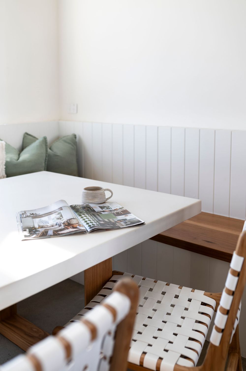 Minimalist cafe interior with built-in white bench seating, wooden accent panel, and white walls in natural lighting.