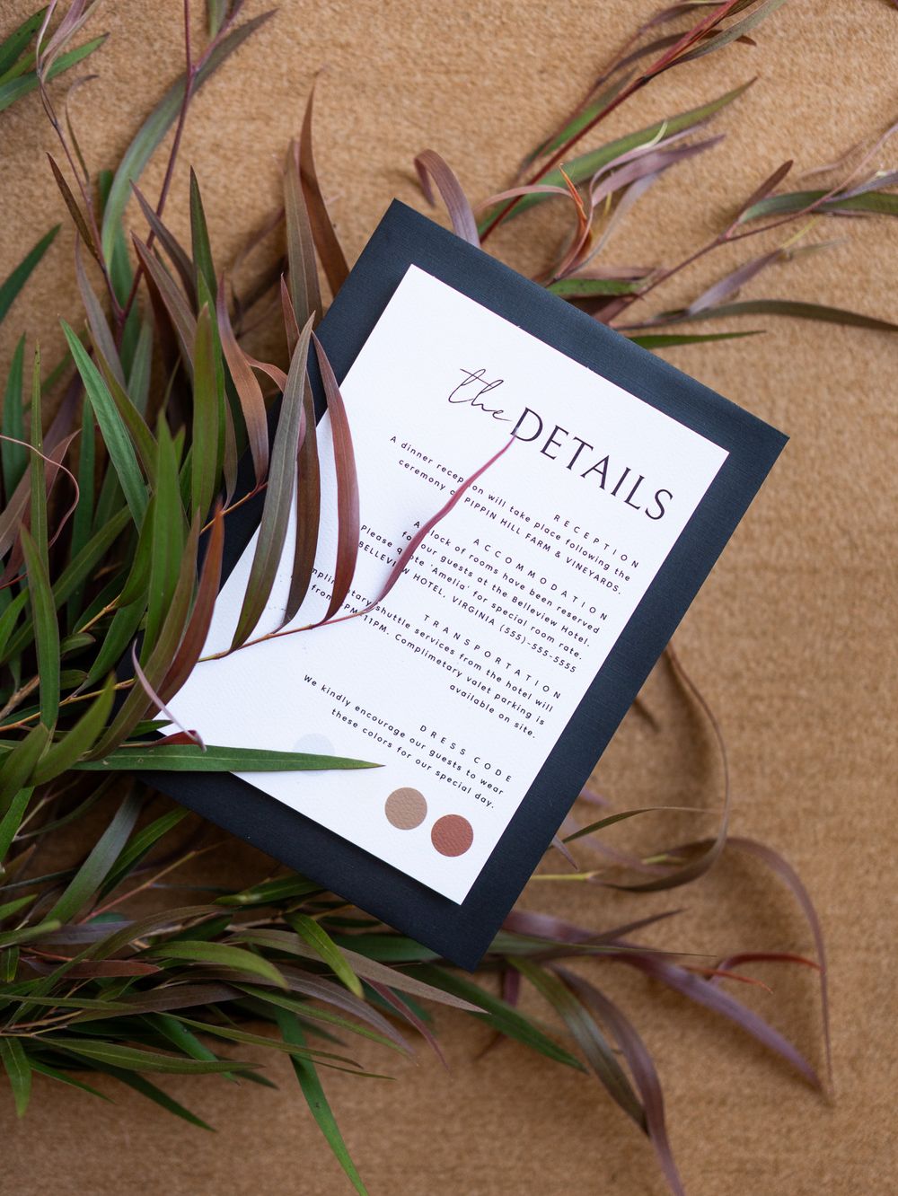 A modern black and white wedding details card with elegant typography styled with eucalyptus leaves on beige paper.