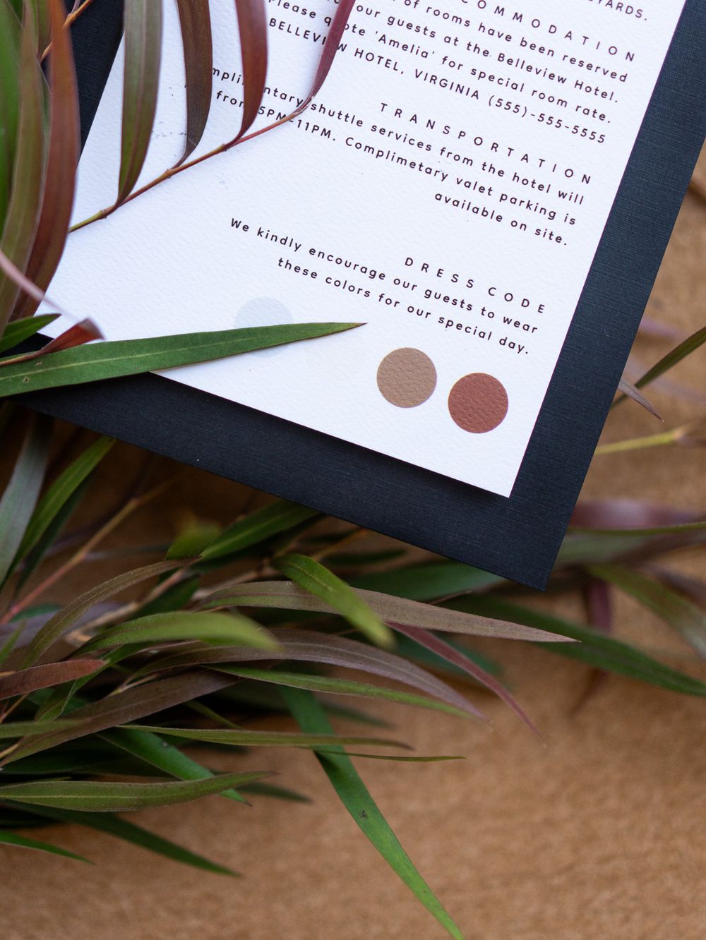 A white wedding invitation with minimalist design featuring copper metallic dots rests against green palm fronds.