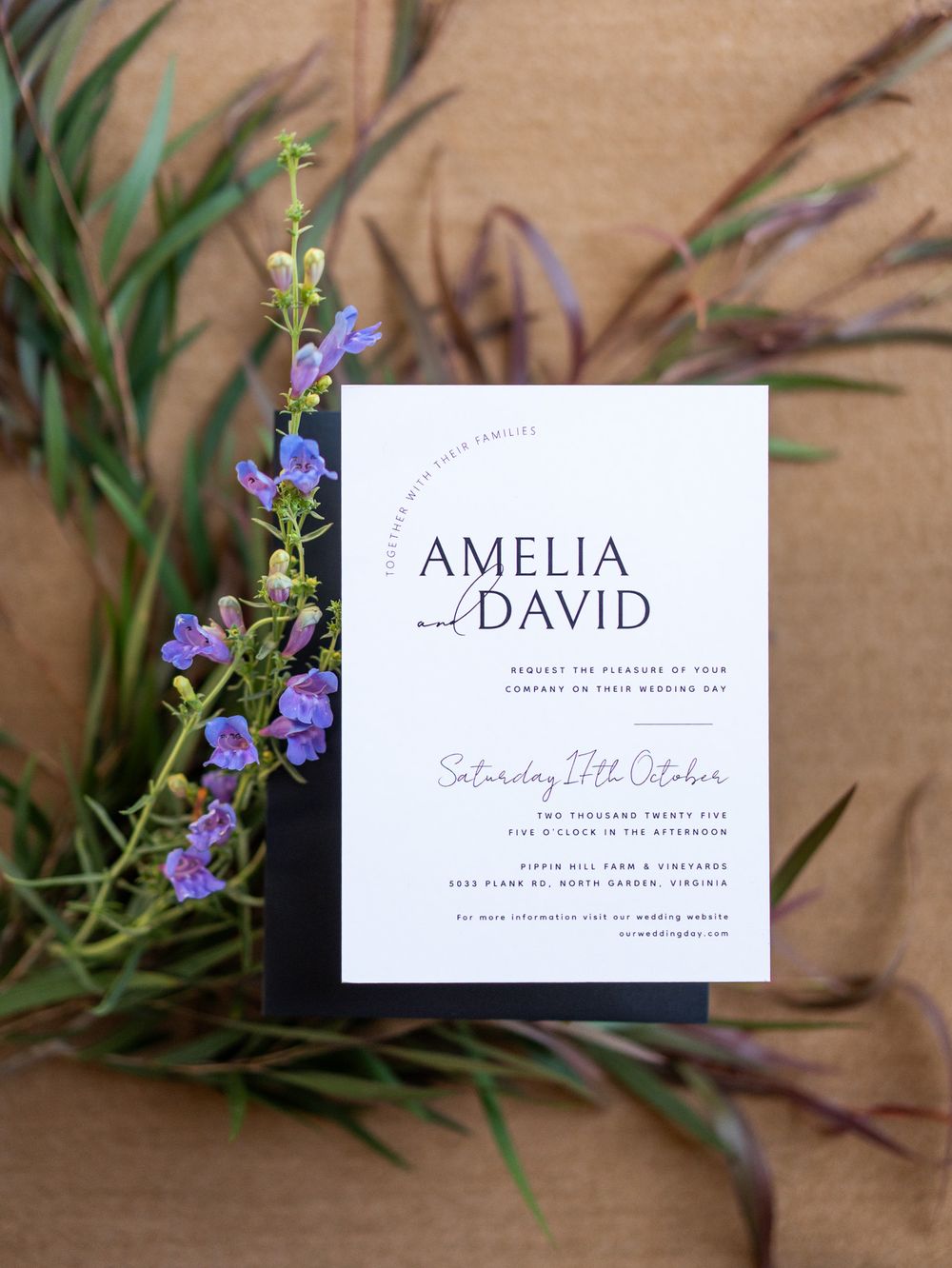 Modern minimalist wedding invitation with purple flowers and greenery on a natural textured background.