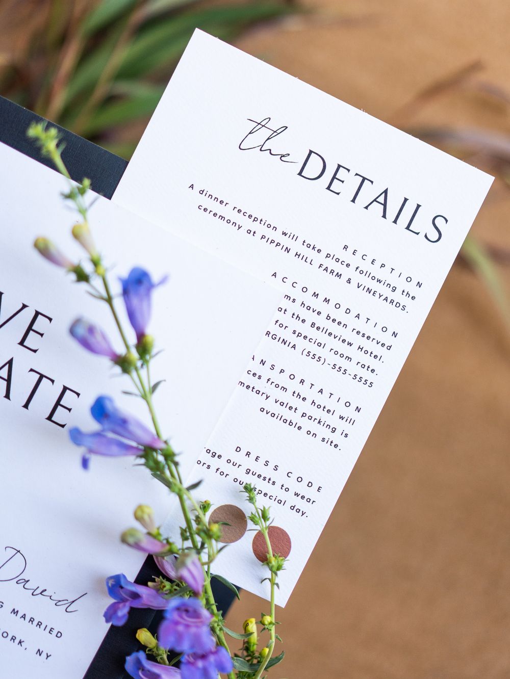White wedding details card with purple wildflowers and foliage against a neutral background showing event information.