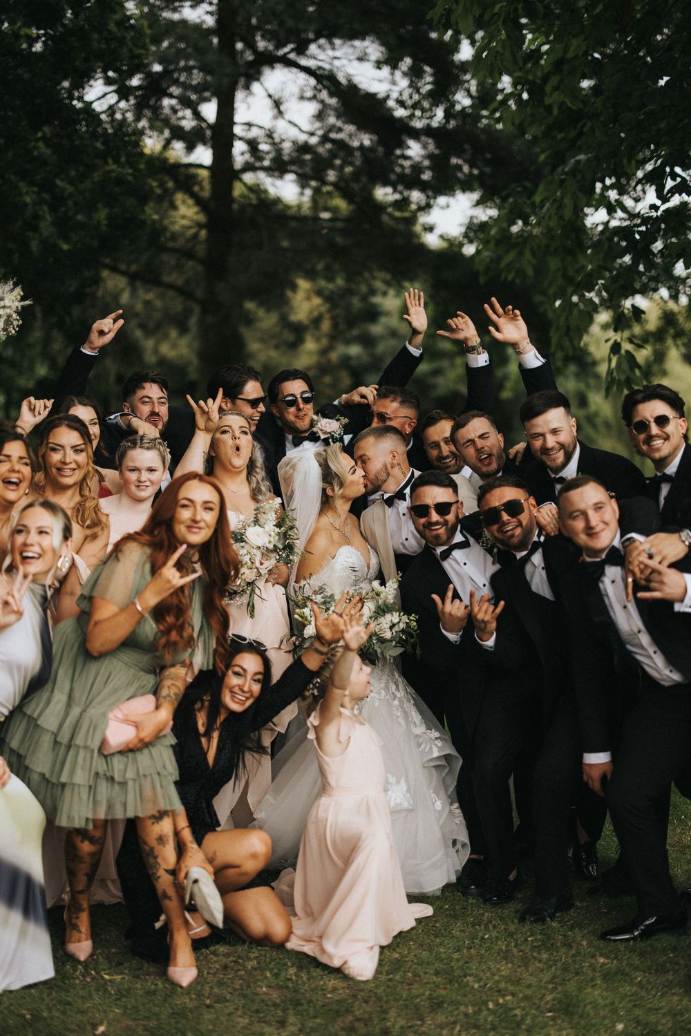 Wedding party group photo showing fun celebration with bridesmaids in sage dresses and groomsmen in dark suits.