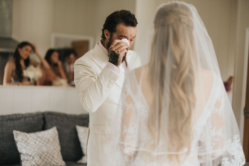 An emotional first look moment between a groom in white and his veiled bride at their wedding celebration.