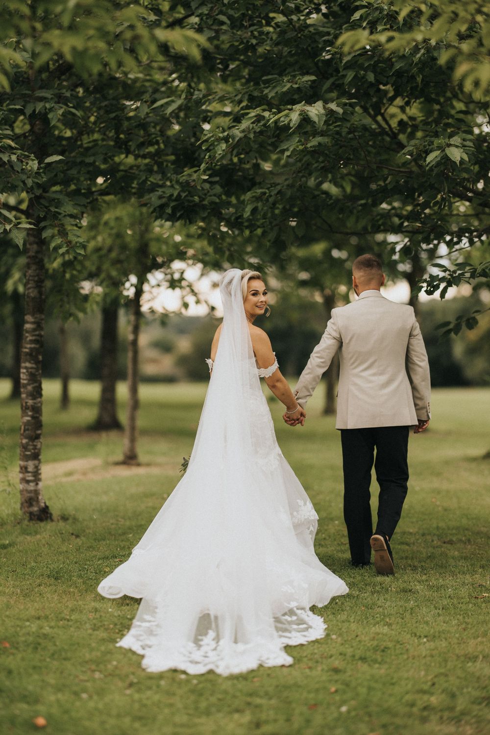 A bride and groom walking together on lush grass during their outdoor wedding photoshoot.