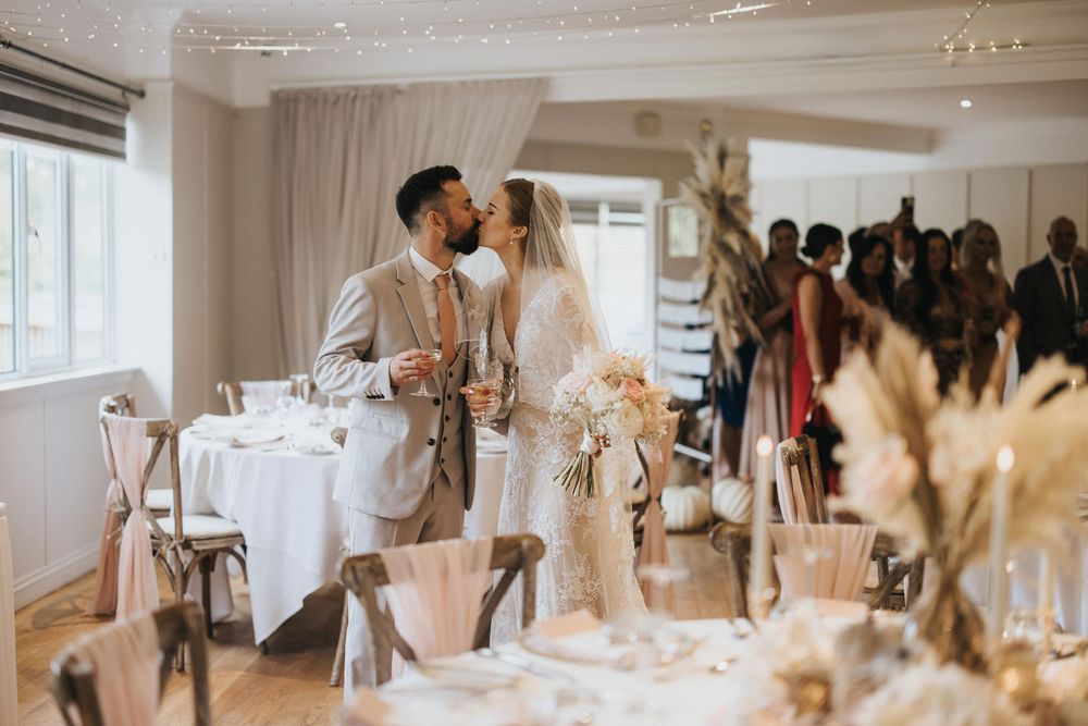 A romantic wedding celebration inside a bright white venue adorned with pampas grass and delicate floral arrangements.
