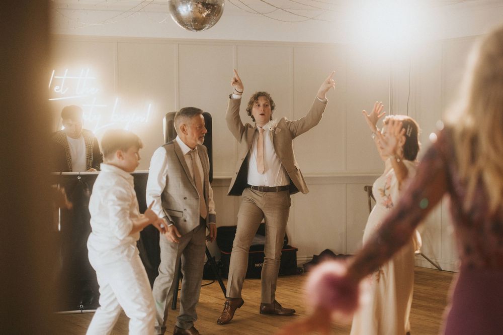 People dancing energetically at a reception with a disco ball overhead in a warm-lit room during a celebration.