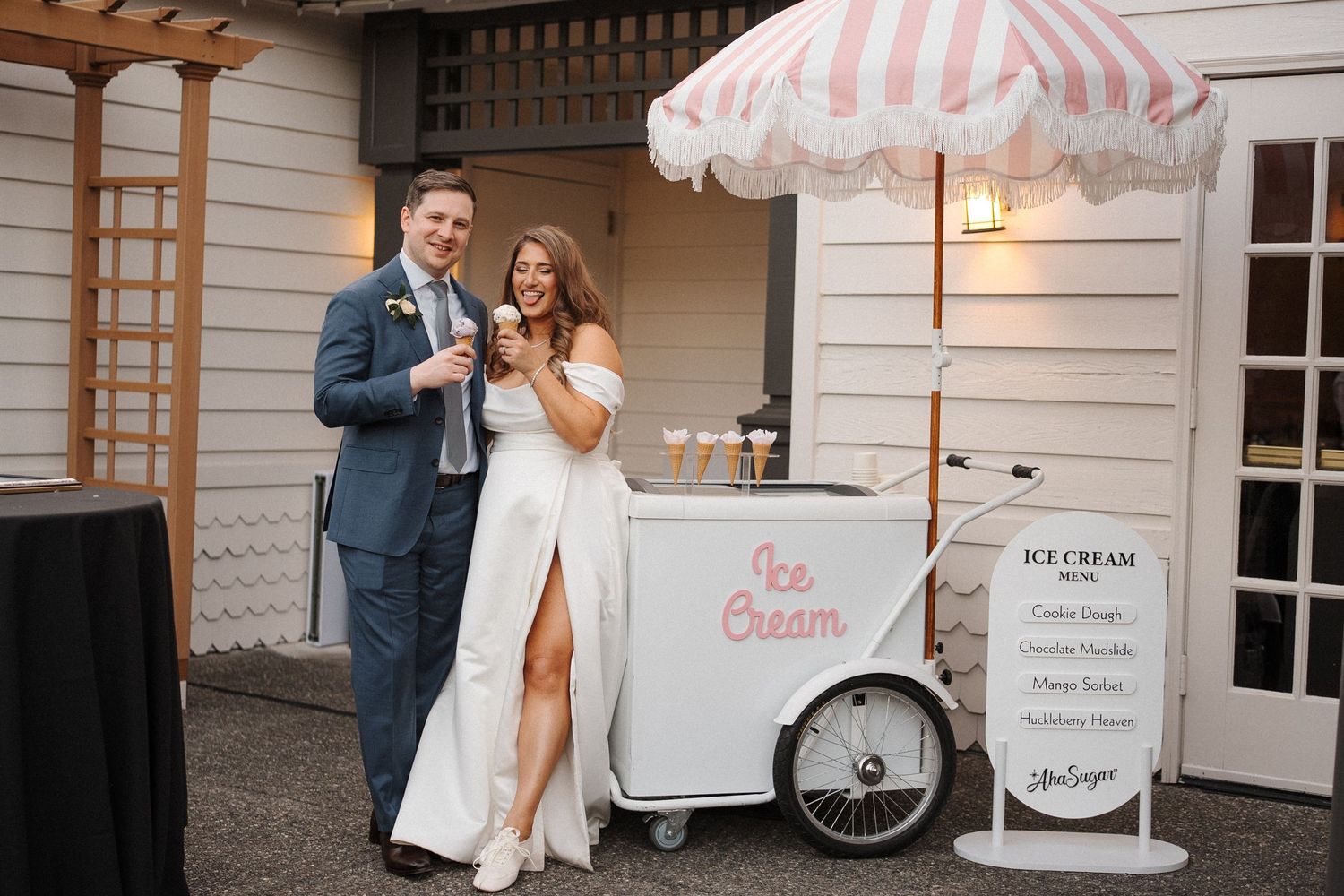 Wedding ice cream cart with pink and white striped awning serves dessert to guests at outdoor reception.