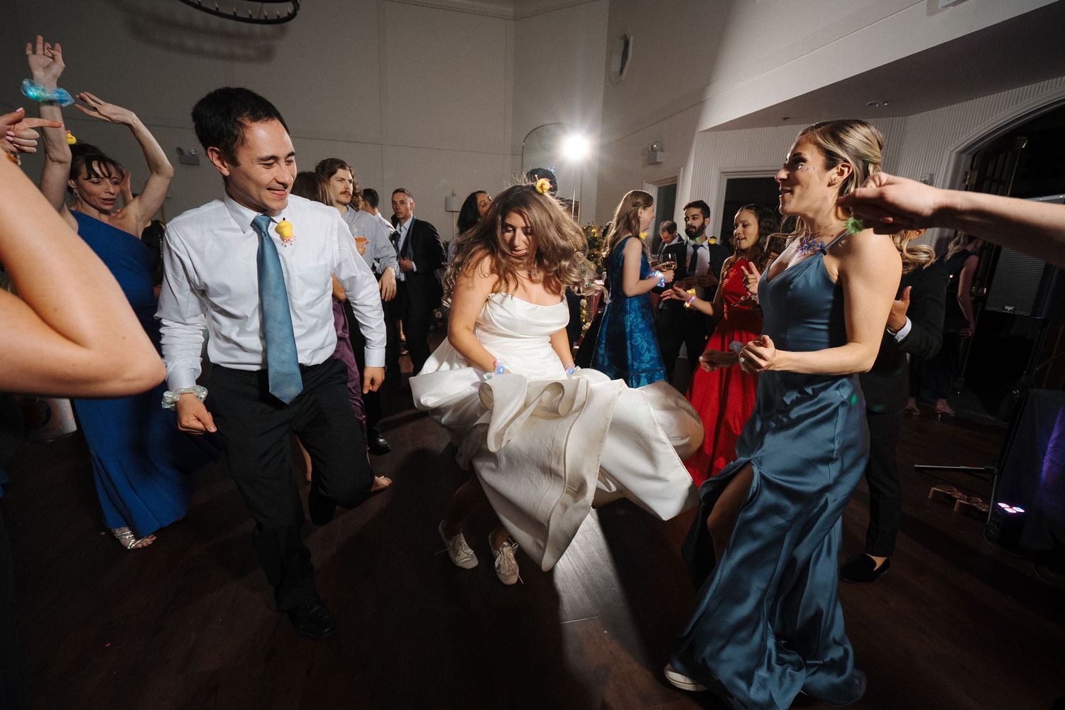 Wedding party guests dance and celebrate together on a dimly lit dance floor during a reception.