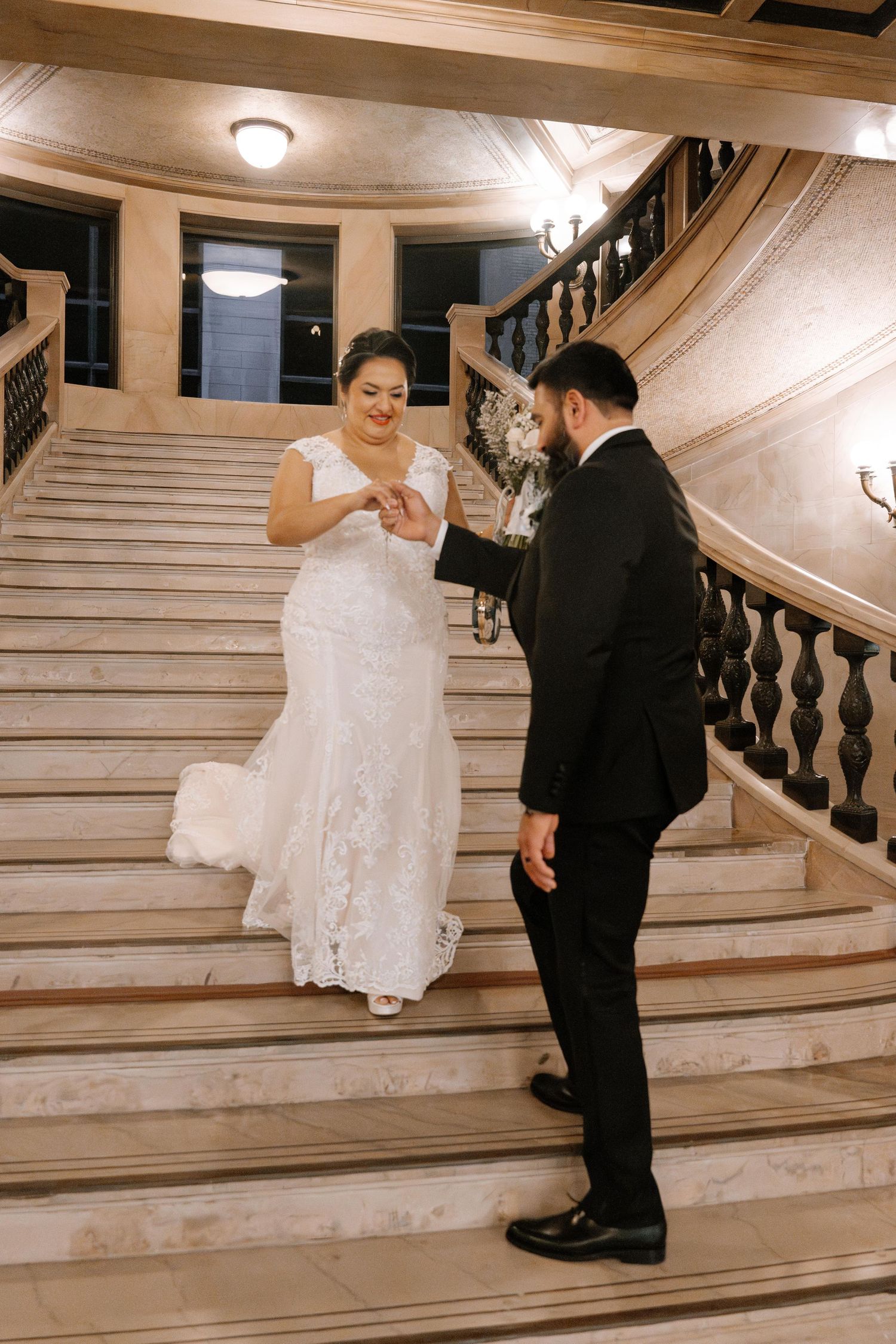 A bride and groom share a romantic dance sequence on an elegant marble staircase in a grand ballroom.