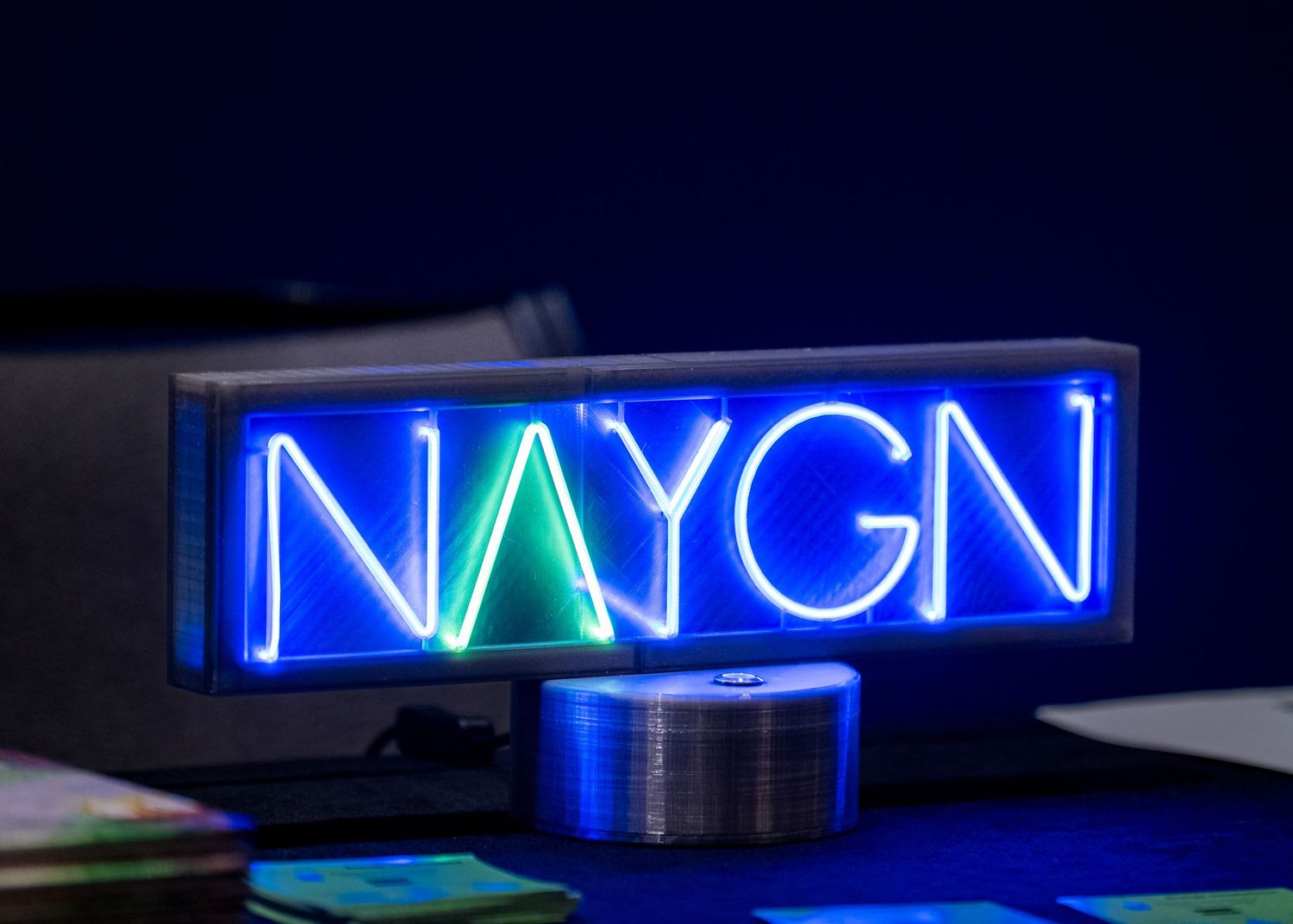 Illuminated blue and green NAYGN neon sign against dark background.