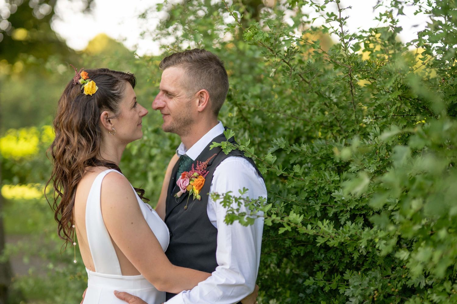 A romantic wedding couple shares tender moments in a lush garden setting surrounded by greenery.