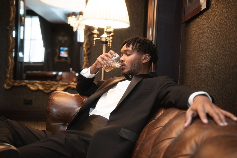 Person in formal attire reclining on dark leather couch in dimly lit room.