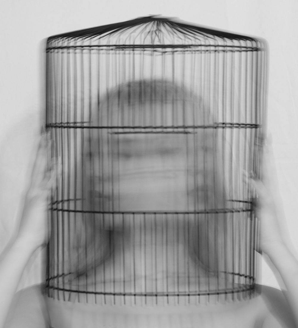 An artistic photo of a woman's head in a bird cage with movement to depict movement.