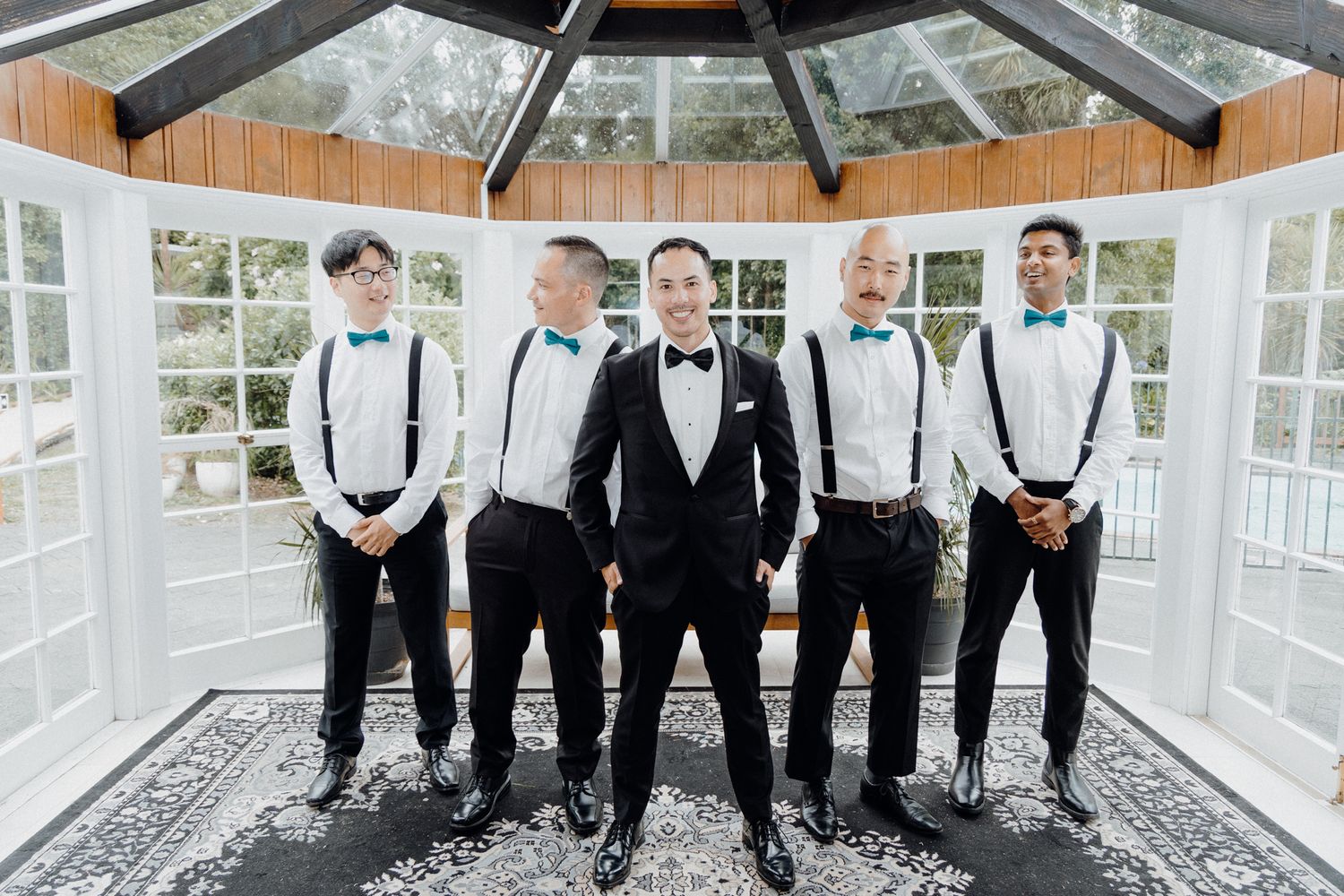 Wedding party in black and white attire standing in elegant sunlit gazebo captured by Apertured Media Auckland Wedding Photographer.