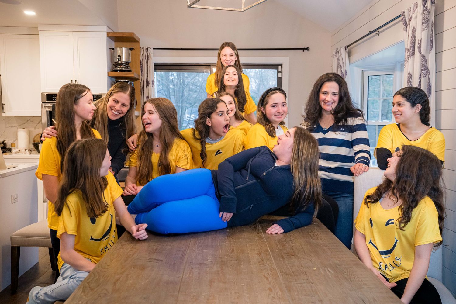 A group wearing yellow shirts laugh together while gathered in a bright kitchen with modern decor.