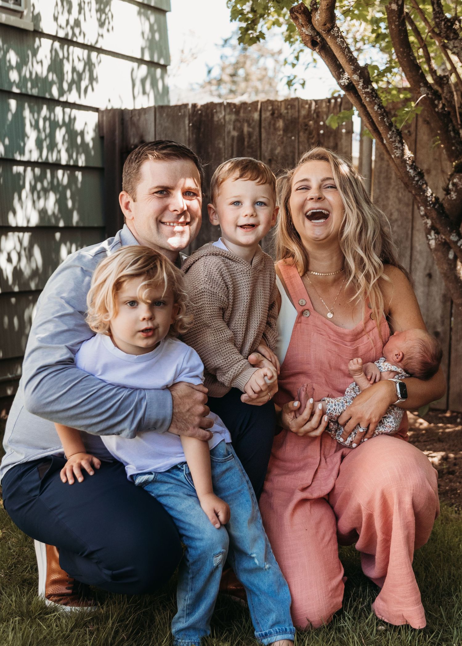 Joyful family posing and laughing together in a backyard garden setting.