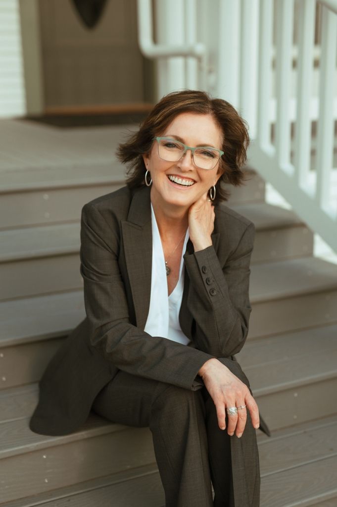 Professional in a dark business suit sits casually on wooden steps with a bright, welcoming expression.