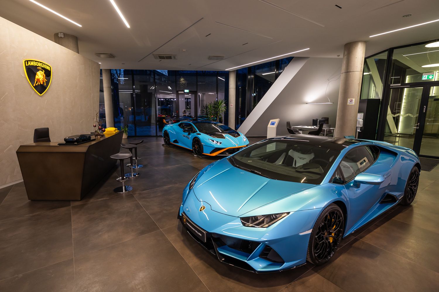 Two light blue Lamborghini sports cars displayed in a modern luxury car dealership showroom with minimalist interior design.