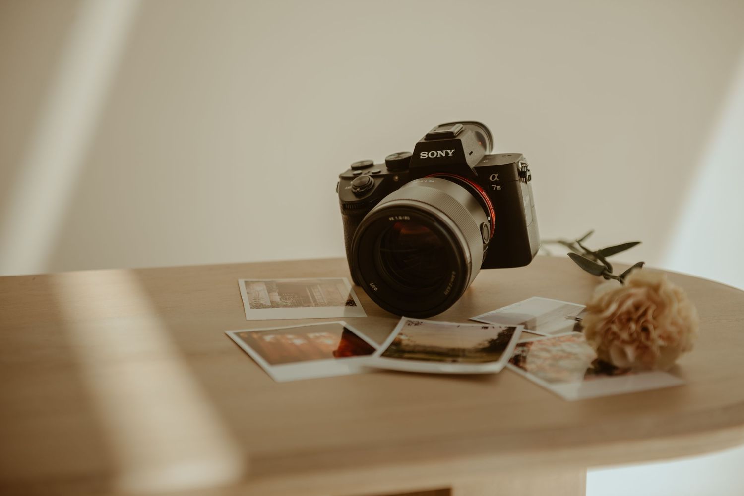 A vintage-style camera sits on a wooden table beside scattered photographs in warm, moody lighting.