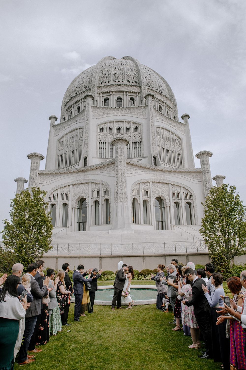 A wedding ceremony takes place in front of the majestic Baha'i House of Worship in Chicago with guests lining the pathway.
