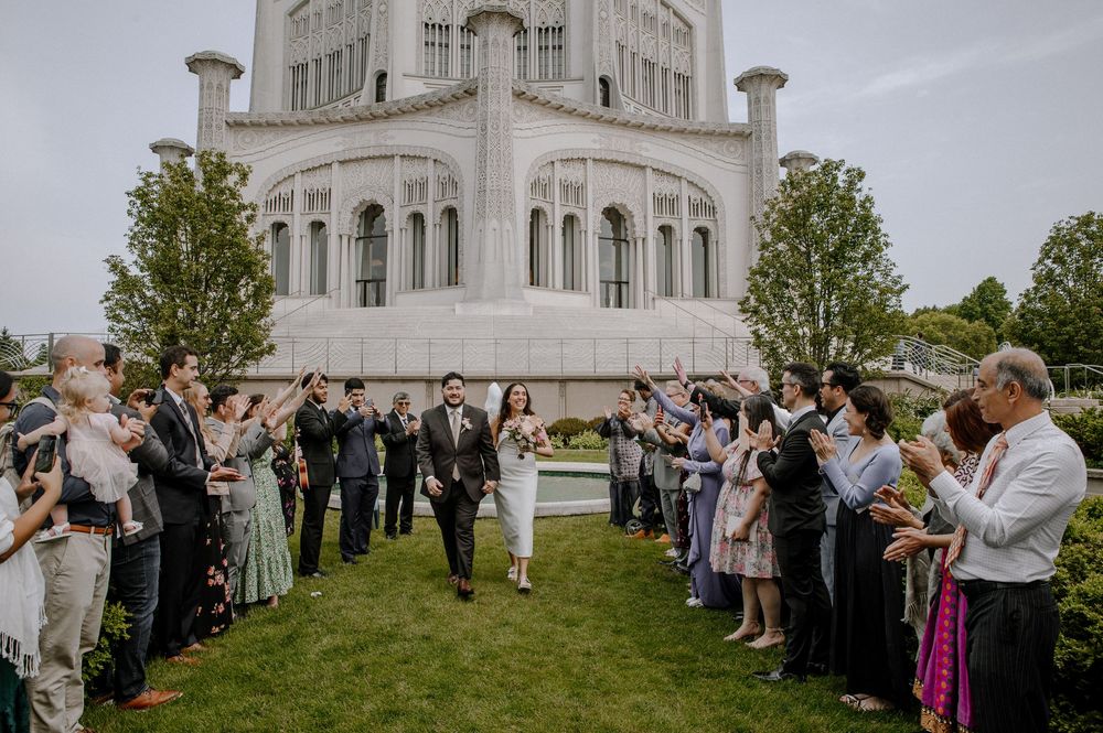 A crowd celebrates a couple's special moment outside a white church building with bubbles floating in the air.